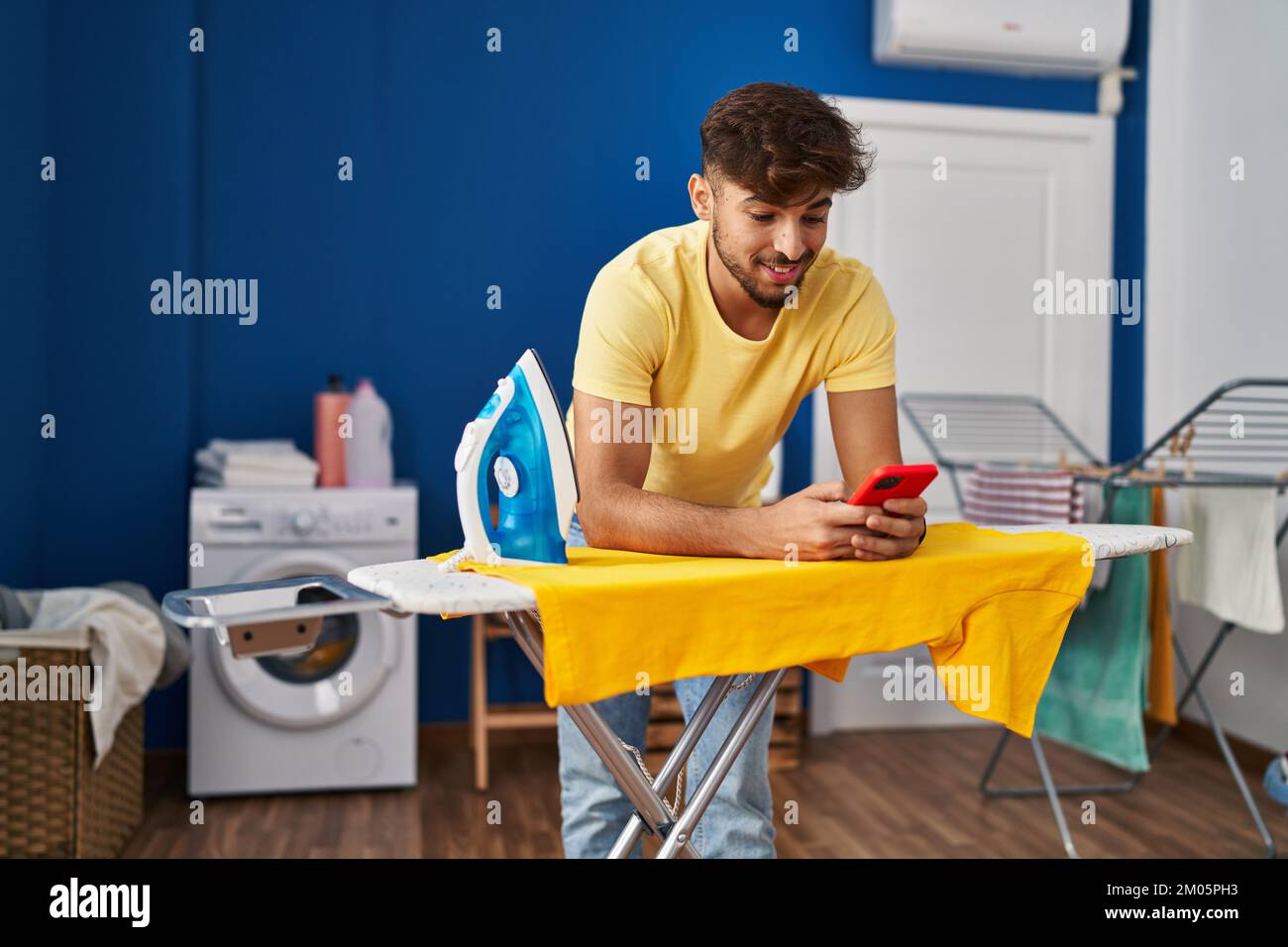 Young arab man using smartphone ironing clothes at laundry room Stock ...