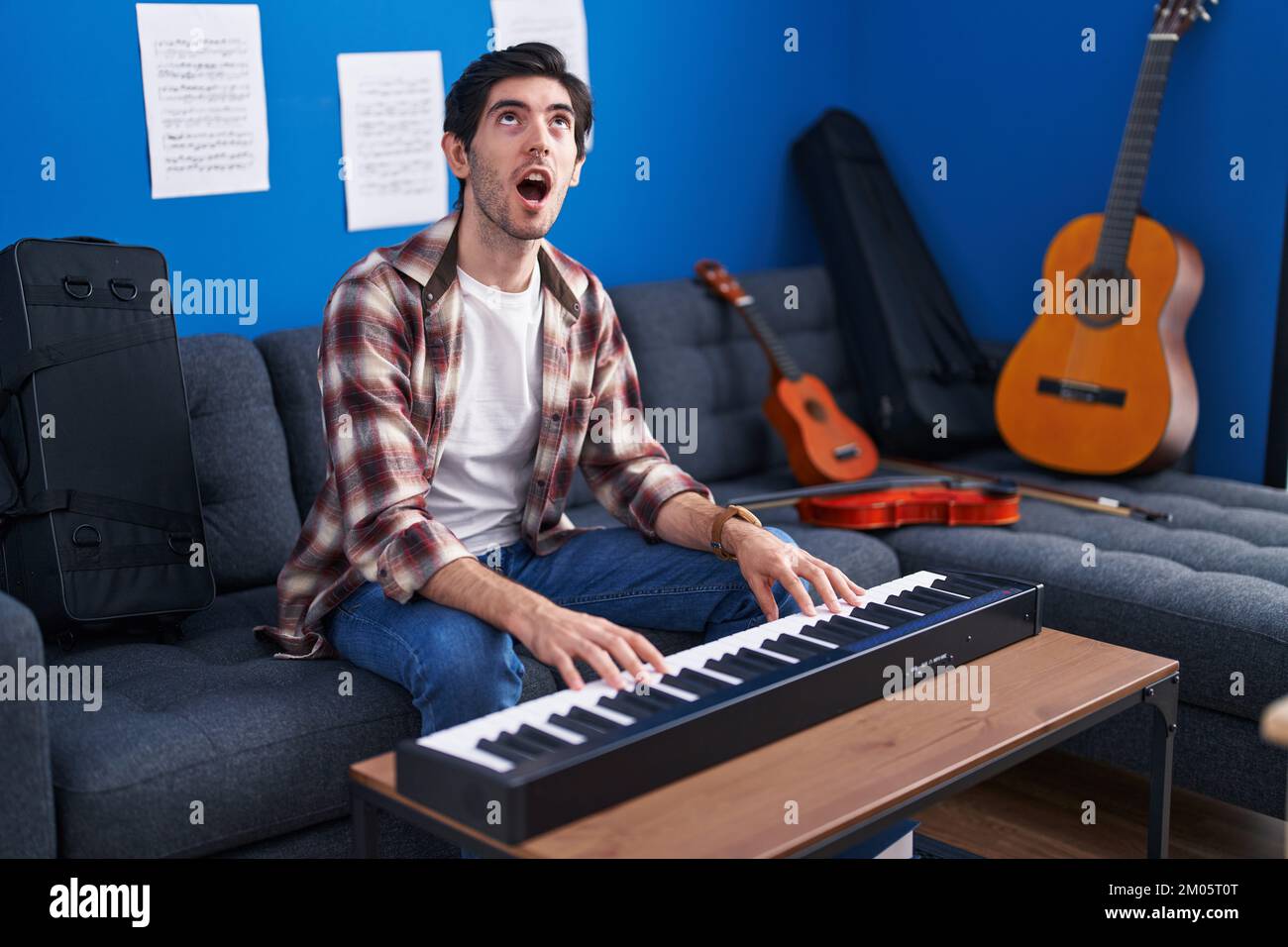 Young hispanic man playing piano at music studio angry and mad screaming  frustrated and furious, shouting with anger looking up Stock Photo - Alamy