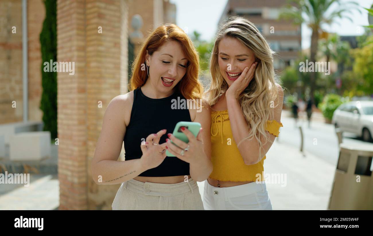 Two women standing together using smartphone at street Stock Photo - Alamy