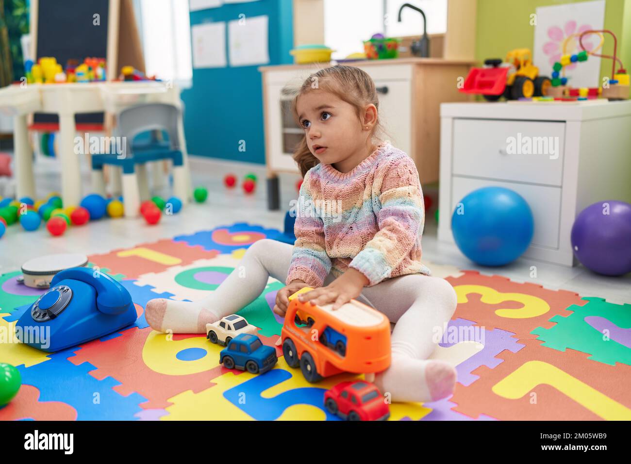 Adorable hispanic girl playing with car toy sitting on floor at ...