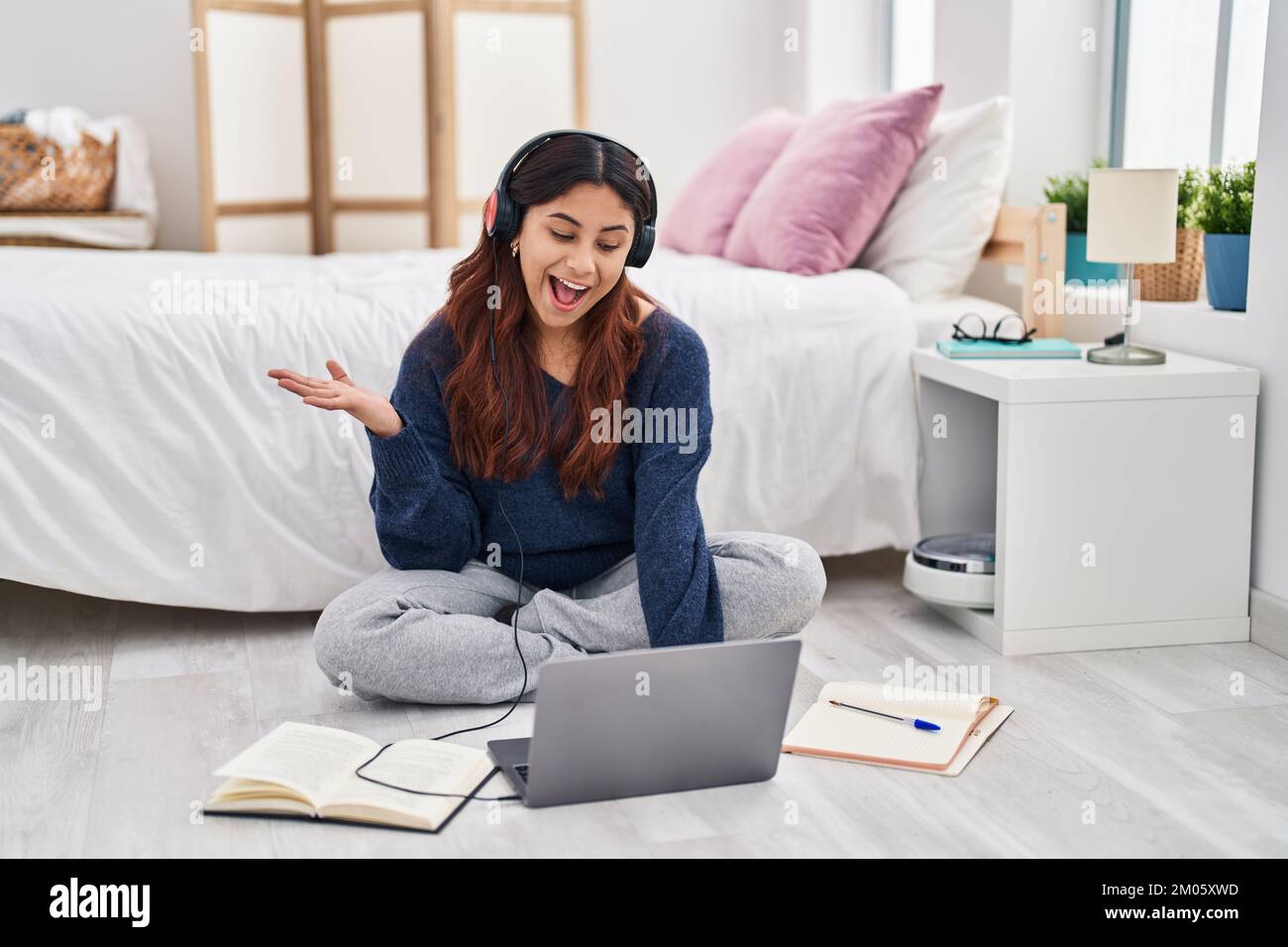 Hispanic young woman using laptop sitting on the floor at the bedroom ...