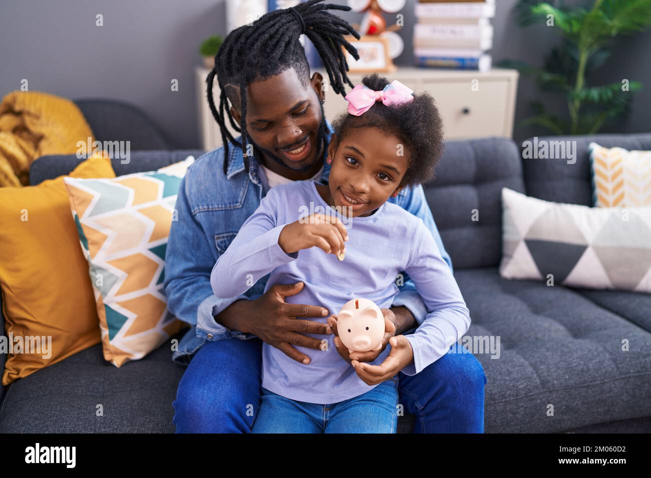 Father and daughter inserting coin on piggy bank sitting on sofa at ...