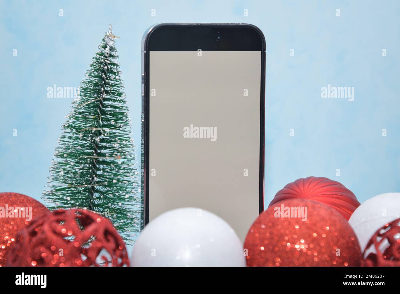 Riga/Latvia-December 4, 2022: new modern phone- Iphone 14 pro white screen. Glittering Christmas decorations on a blue background. Christmas gift conc Stock Photo