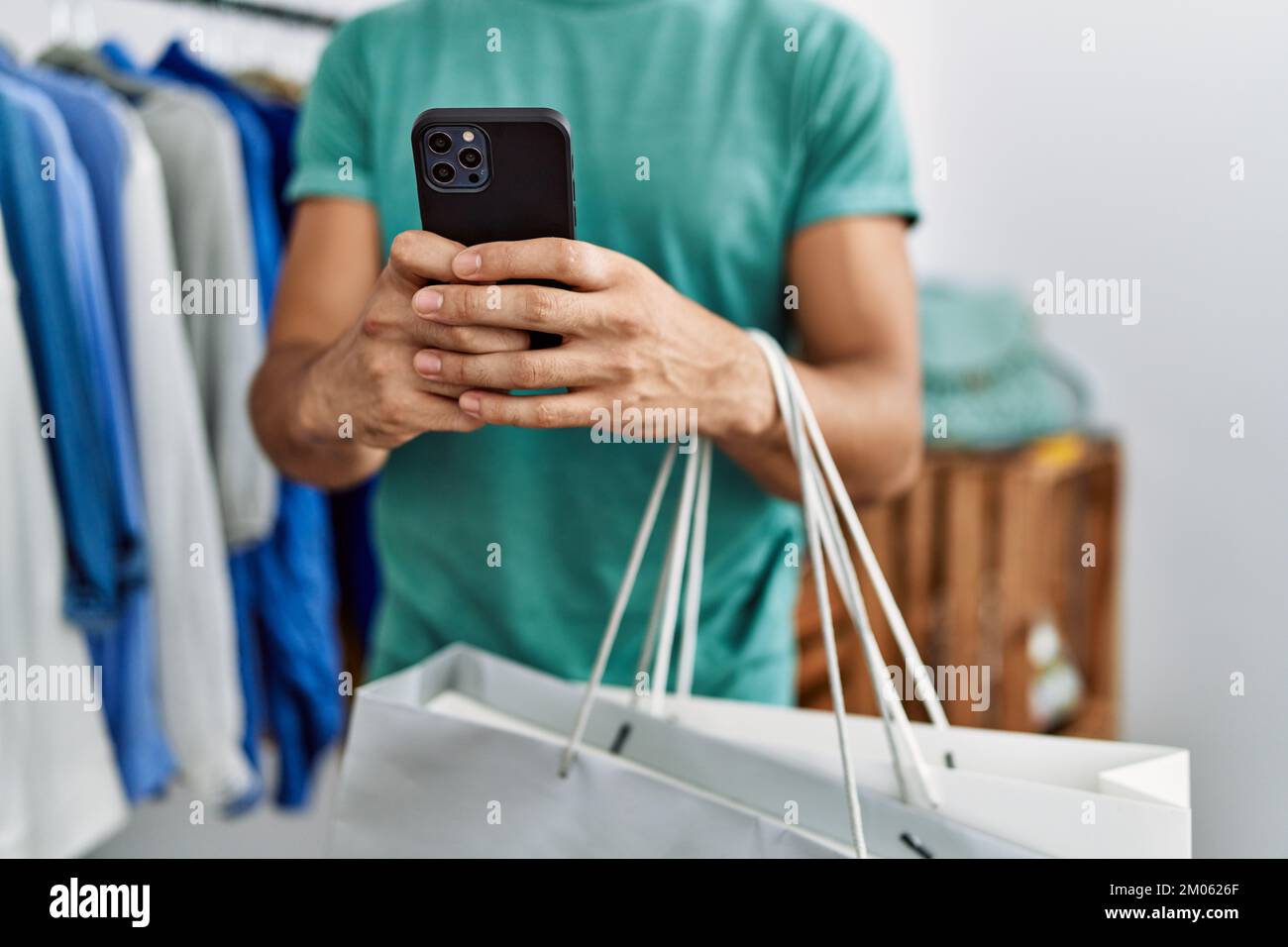 Young arab man customer using smartphone holding shopping bags at ...