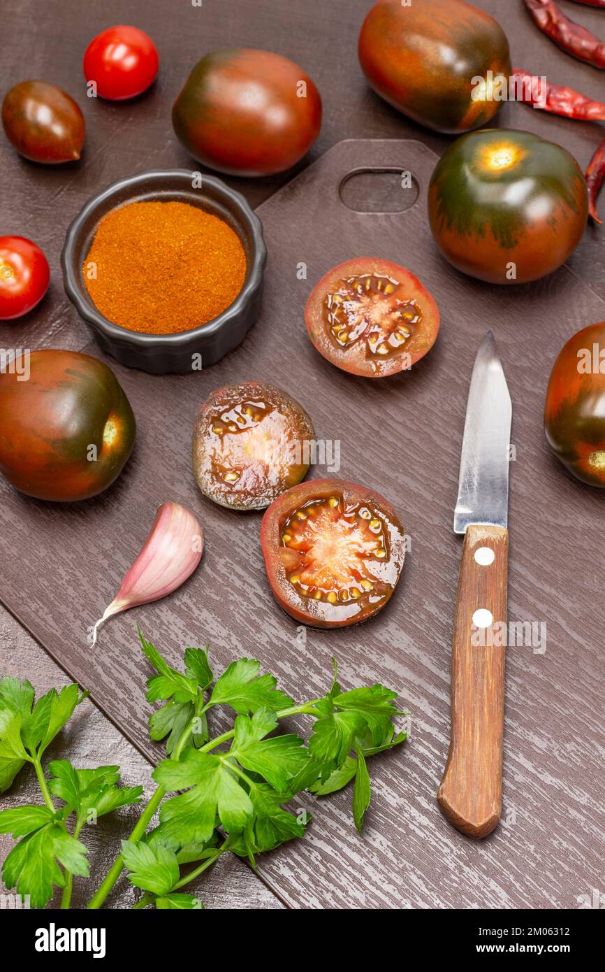 Knife and halves of a tomato. Whole tomatoes on table, paprika in bowl. Top view. Brown background. Stock Photo