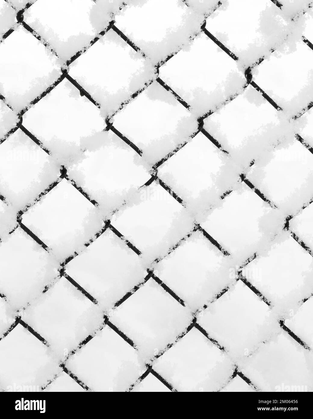 Snow piled on the wire of a diamond pattern mesh black fence in closeup during winter Stock Photo