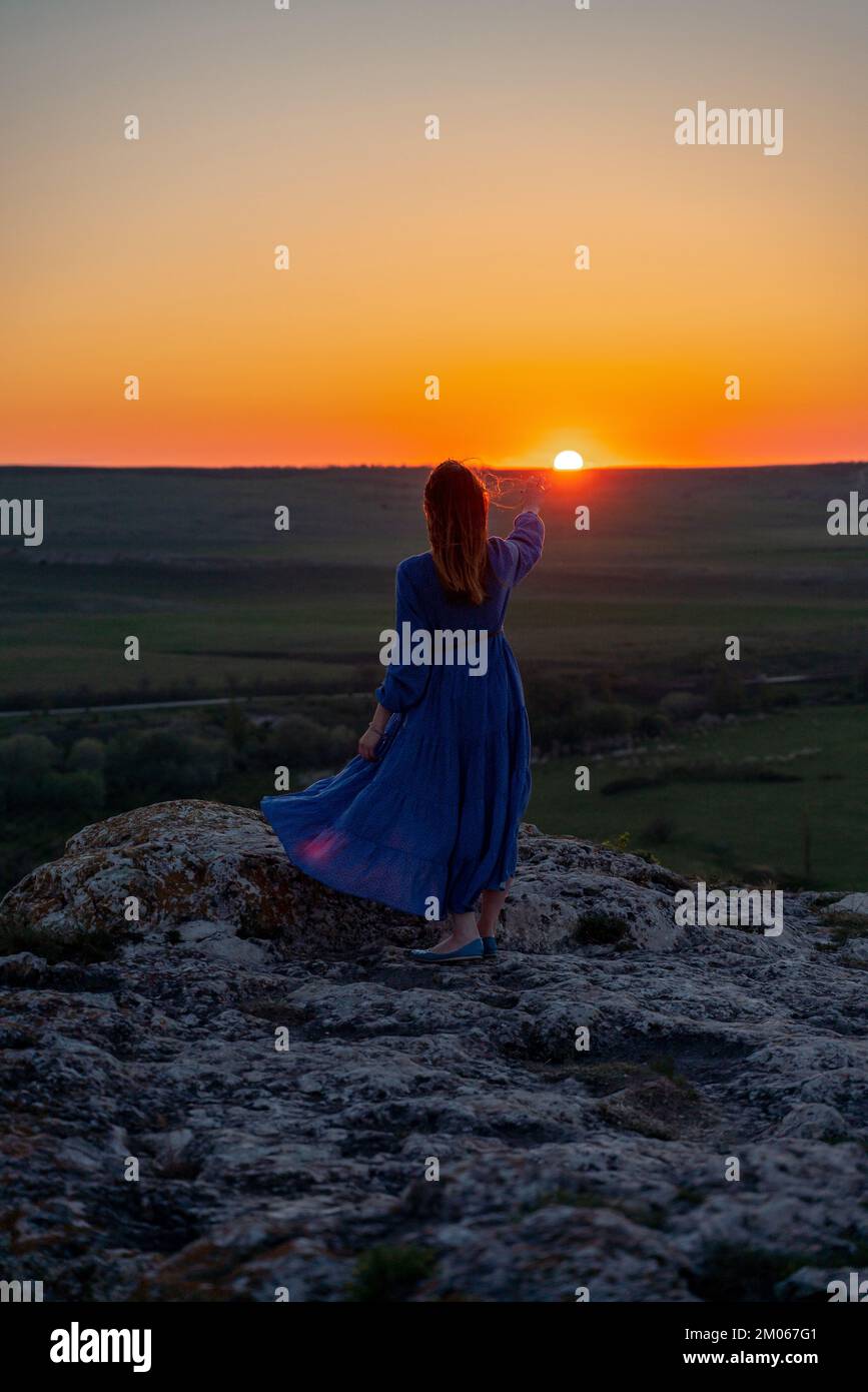 Silhouette of a girl in a blue dress standing on a rock in the ...