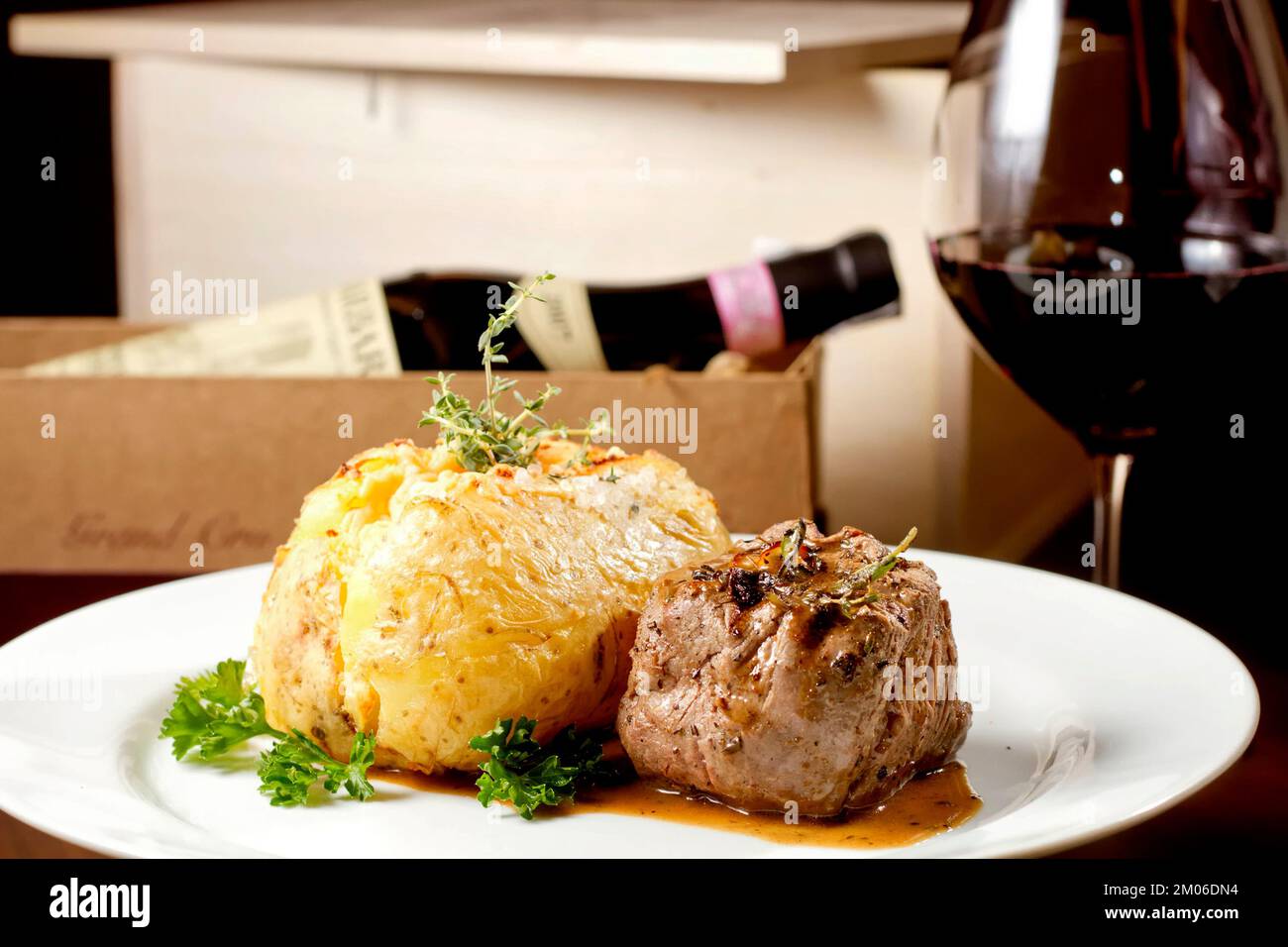 Filet mignon beef steak with gravy and stuffed potato served on a plate paired with red wine glass and bottle. Premium quality restaurant Gourmet food Stock Photo