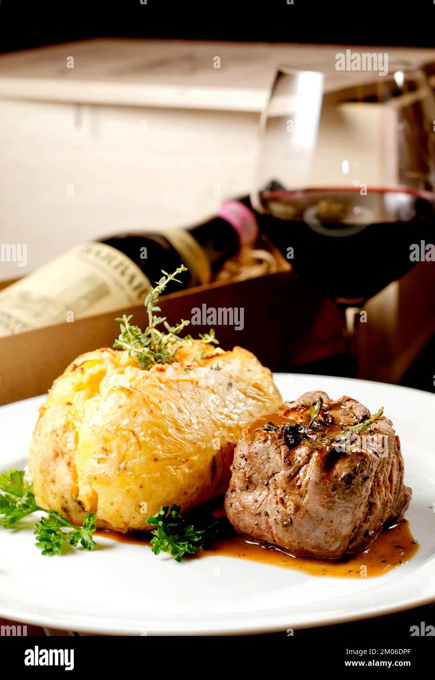 Filet mignon beef steak with gravy and stuffed potato served on a plate paired with red wine glass and bottle. Premium quality restaurant Gourmet food Stock Photo