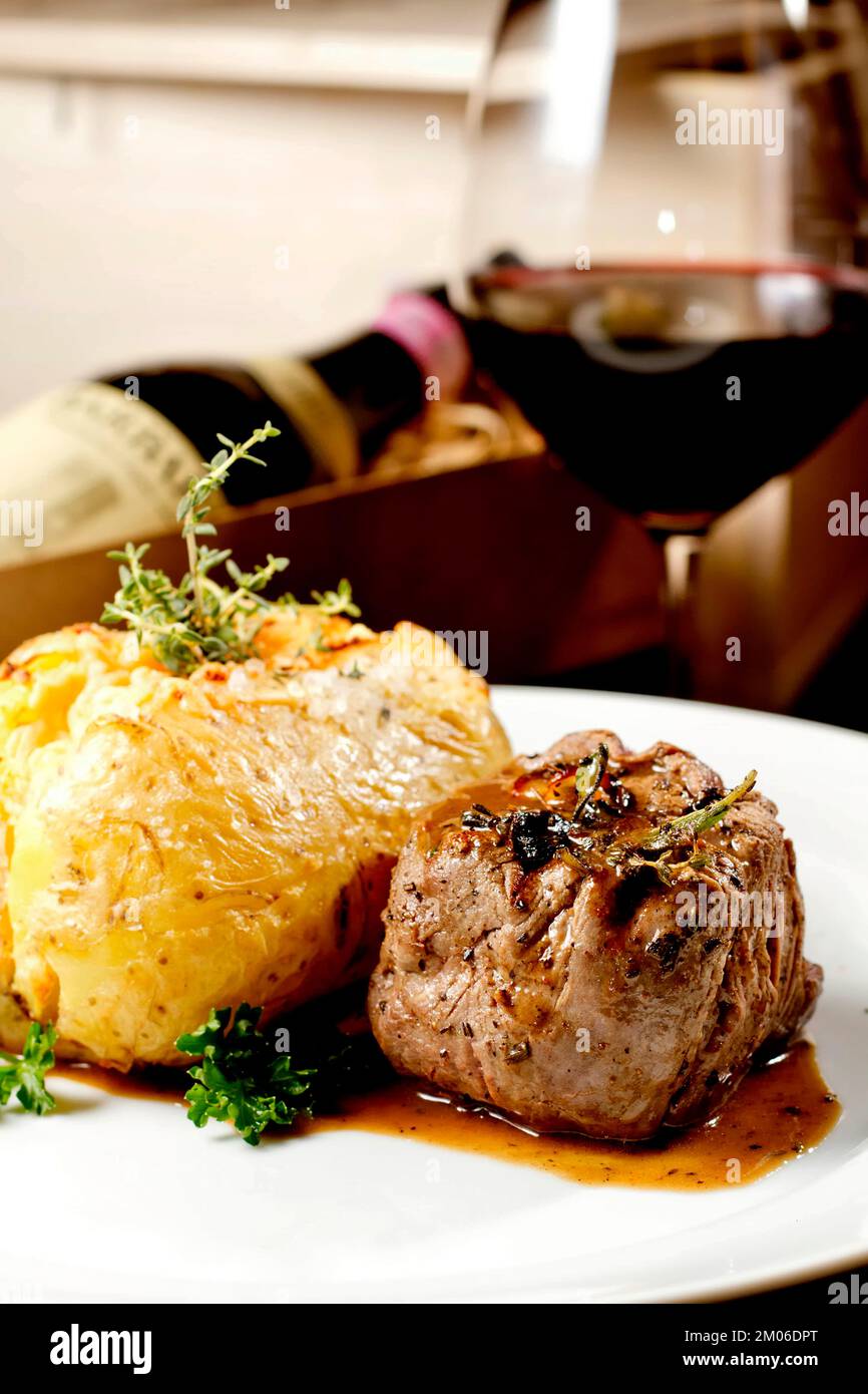 Filet mignon beef steak with gravy and stuffed potato served on a plate paired with red wine glass and bottle. Premium quality restaurant Gourmet food Stock Photo