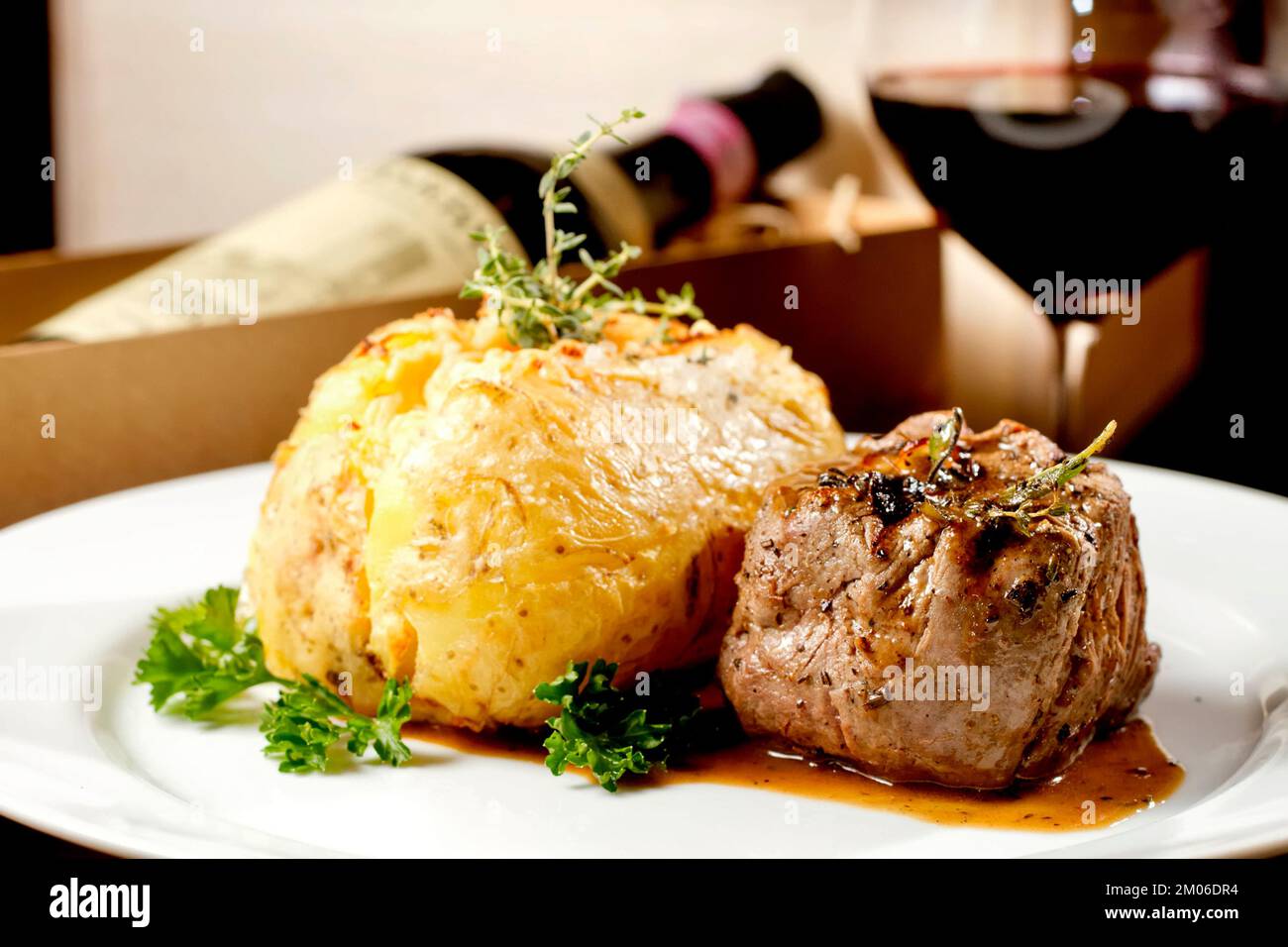 Filet mignon beef steak with gravy and stuffed potato served on a plate paired with red wine glass and bottle. Premium quality restaurant Gourmet food Stock Photo