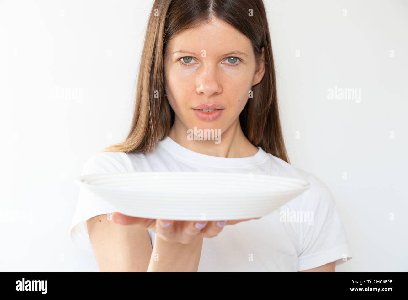 The girl is holding an empty white plate on a white background, the waiter with a plate Stock Photo