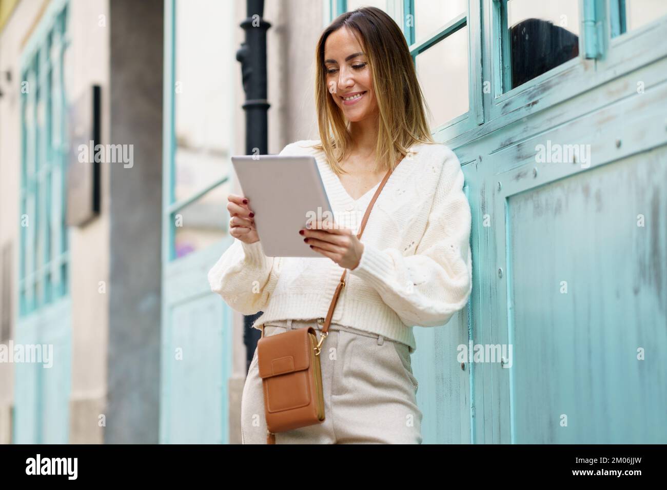 Cheerful woman with tablet standing on street Stock Photo