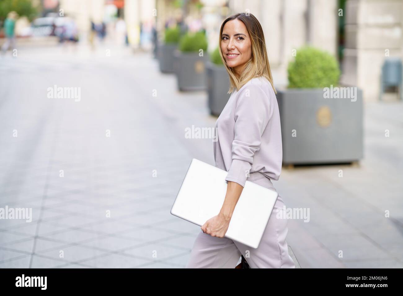 Happy female manager with laptop walking on street before meeting Stock Photo
