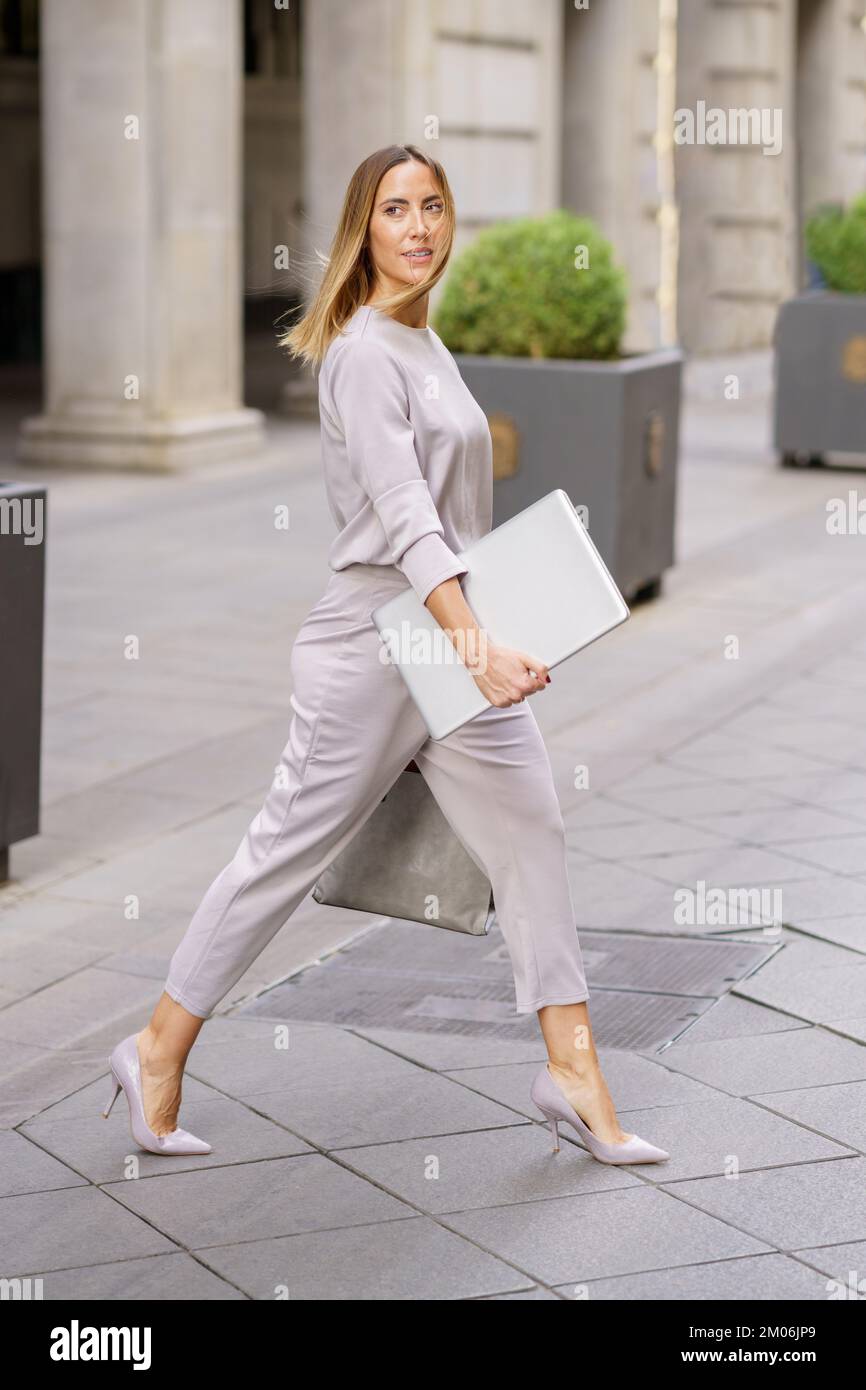 Self assured female manager with laptop crossing street near building Stock Photo