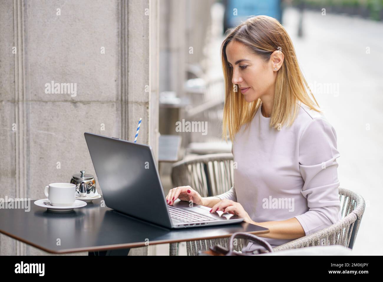 Focused female remote worker using laptop on cafe terrace Stock Photo