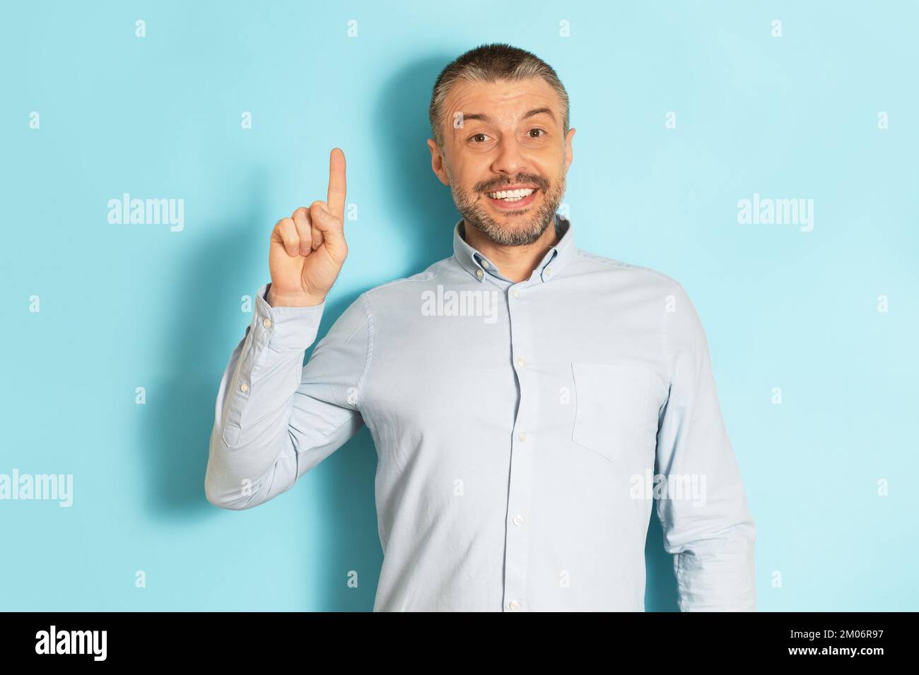 Eureka, gestures concept. Excited mature caucasian man pointing index finger up and smiling over blue studio background Stock Photo