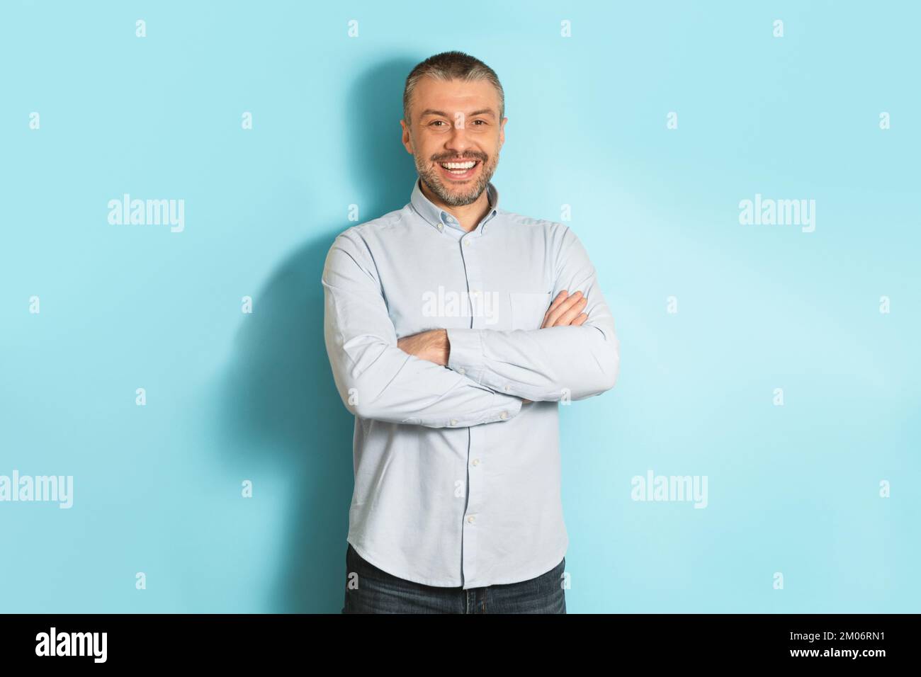 Male portrait. Happy middle aged caucasian man with folded arms smiling at camera, posing over blue studio background Stock Photo