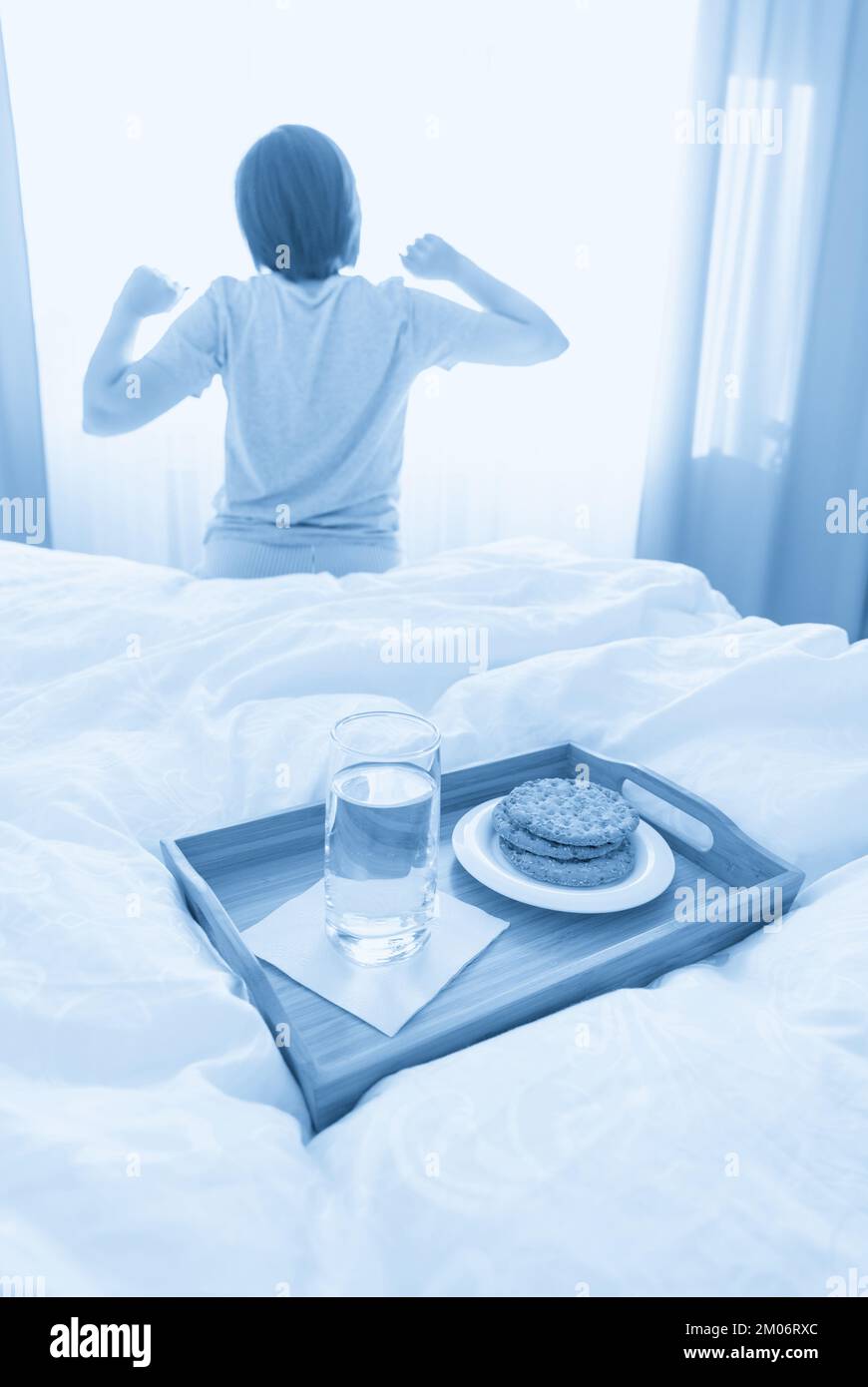 Tray with water and crackers breakfast on a bed with woman stretching
