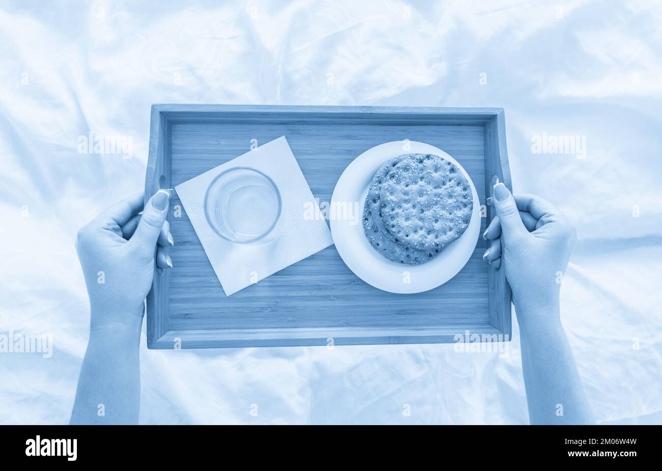 Woman holding tray with diet breakfast of crackers and water on a bed