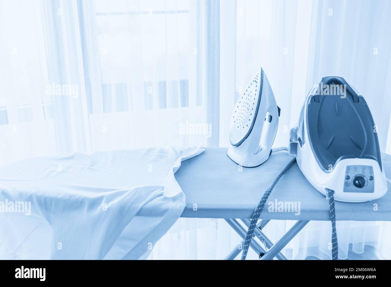 Steaming iron on ironing board near window with copy space Stock Photo