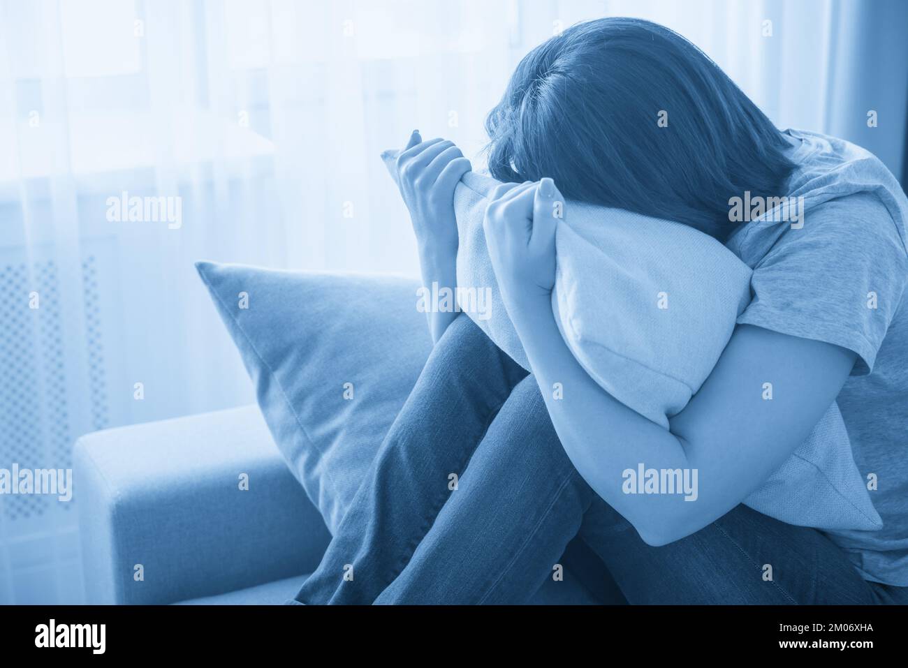 Sad girl sitting on couch and hugging a pillow, loneliness and sadness ...