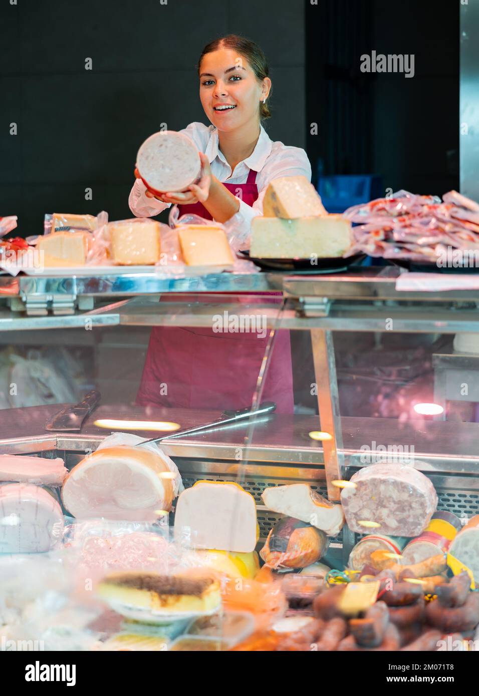 Smiling young girl seller offering fresh mortadella in grocery store