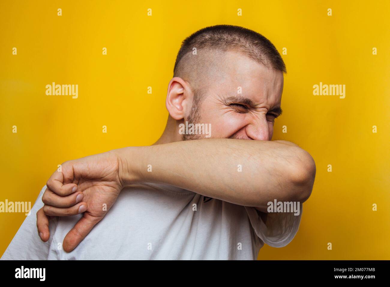 Caucasian man coughs in his elbow and holds hand on chest, experiencing