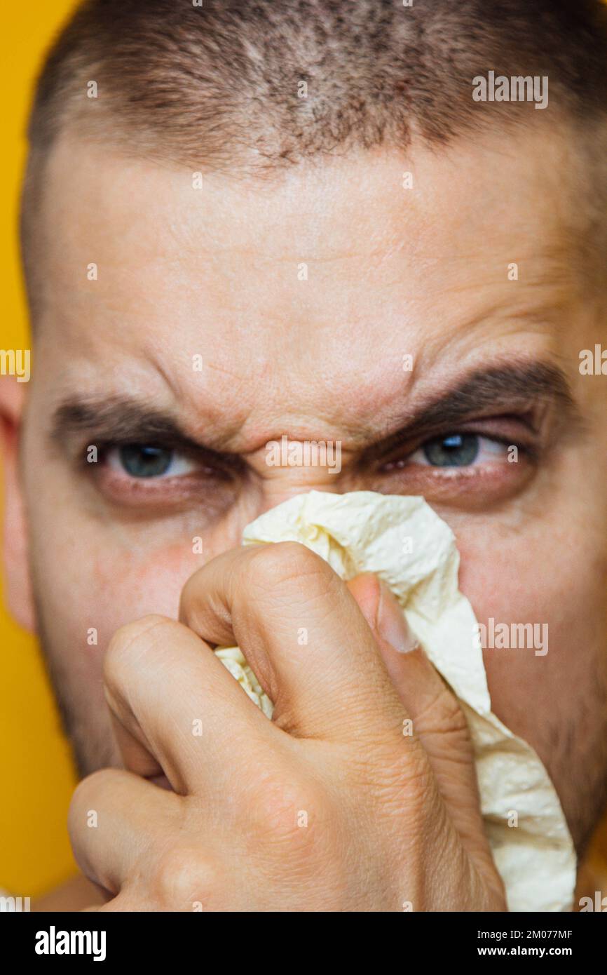 A young guy sick with a virus sneezes into toilet paper that he holds