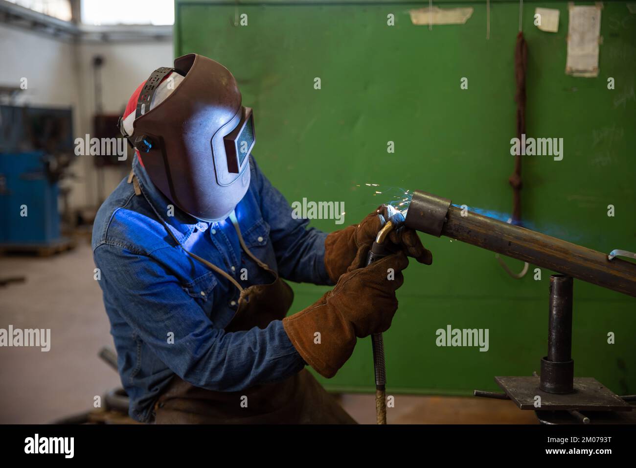 A welder welds a piece of metal in the factory, industrial work Stock