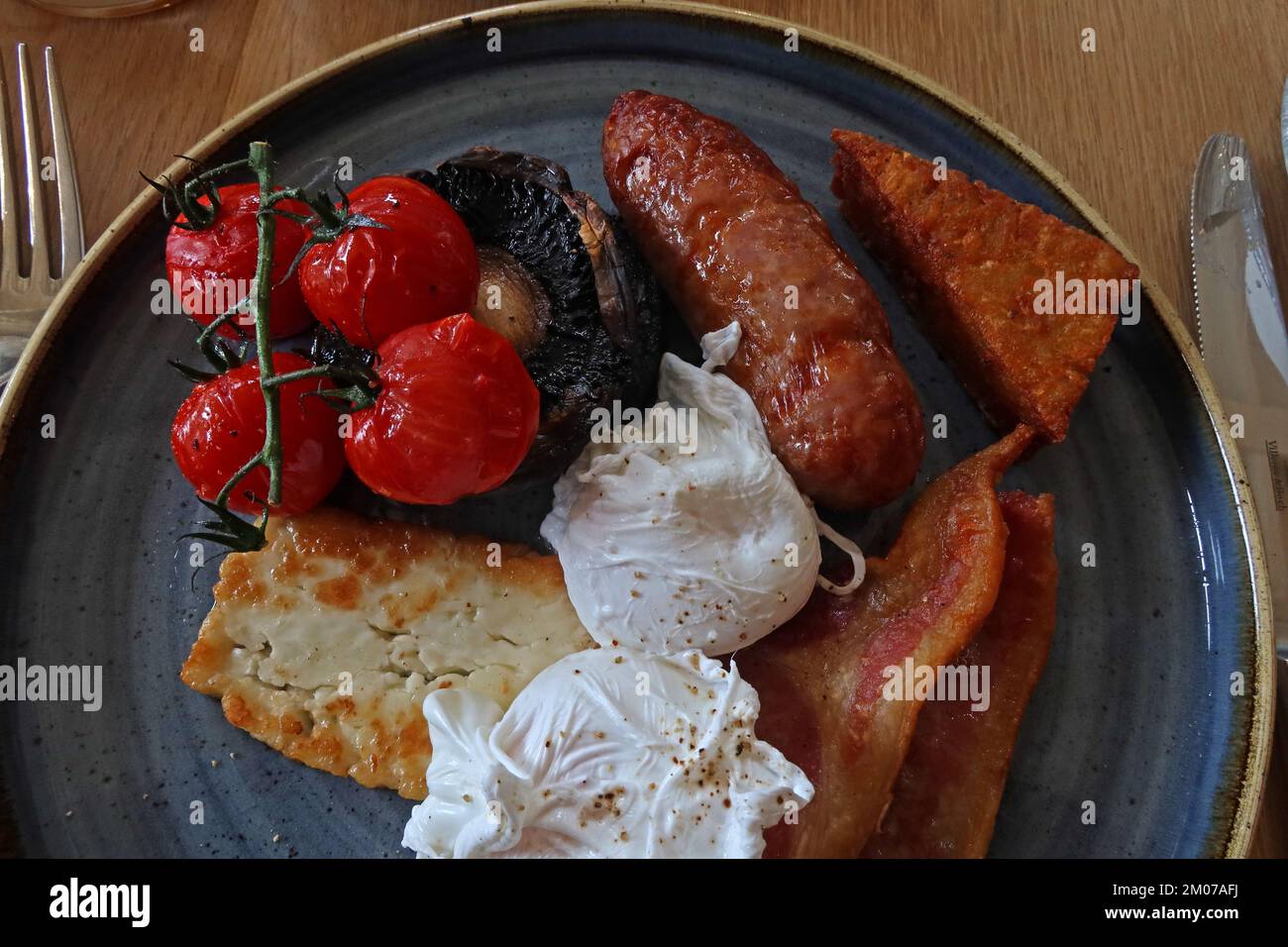Quality hot cooked British breakfast, poached eggs, halloumi, bacon, sausages, hash-brown, fried on the vine tomatoes and mushroom Stock Photo