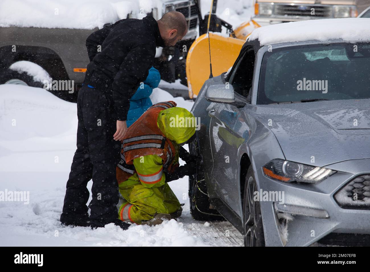 A chain installer works on a vehicle. Heavy snowfall and blizzard like