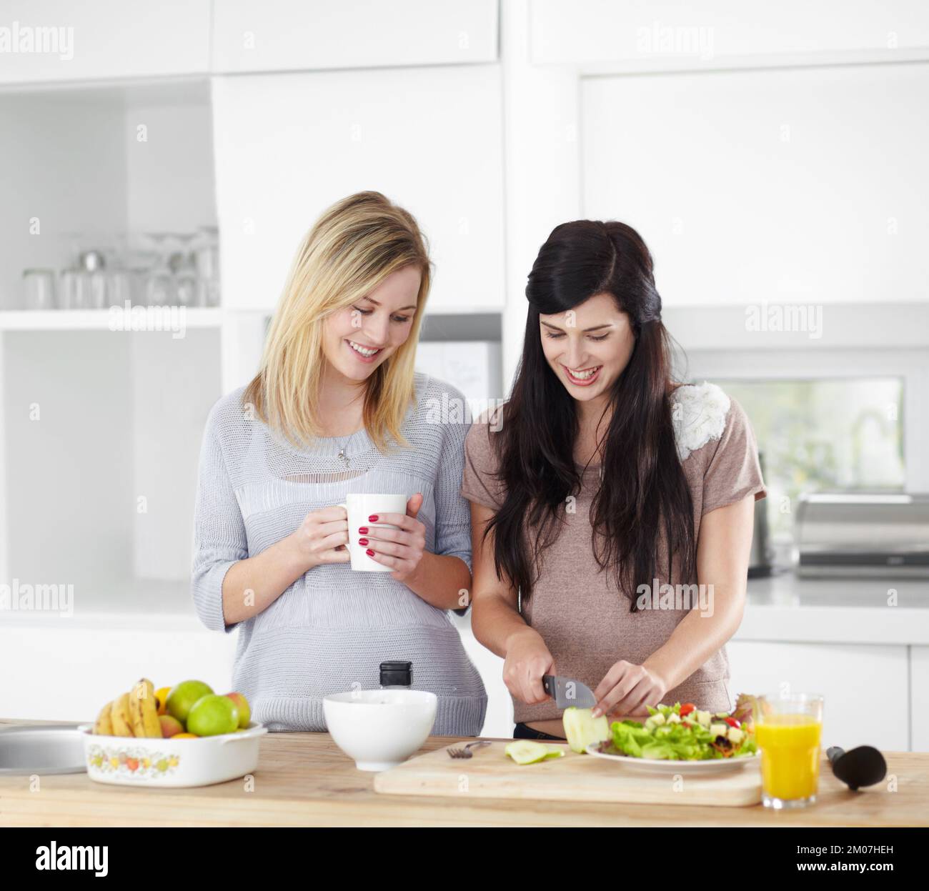 Serving up a healthy meal. Two young women making a salad in the kitchen at home. Stock Photo