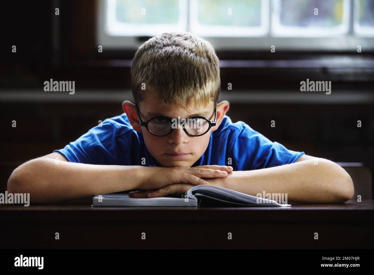 This work is boring. Young boy feeling overcome with boredom in the classroom. Stock Photo