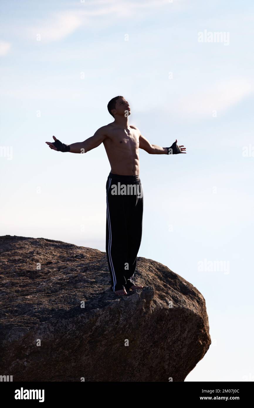 Freedom in the mountains. A male kickboxer looking upwards while standing on a mountain ledge. Stock Photo