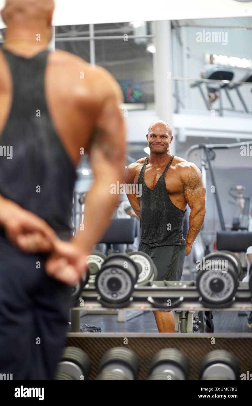 Checking On His Progress A Muscular Bodybuilder Flexing His Muscles While Watching His 1406