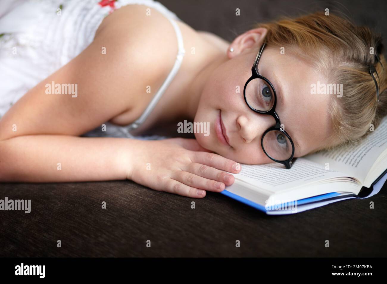 Reading myself to sleep. A young girl wearing glasses lying with her head on her book. Stock Photo