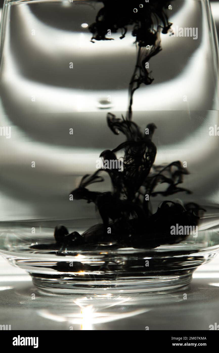a cloud of ink in a transparent glass cup with clear water against the ...