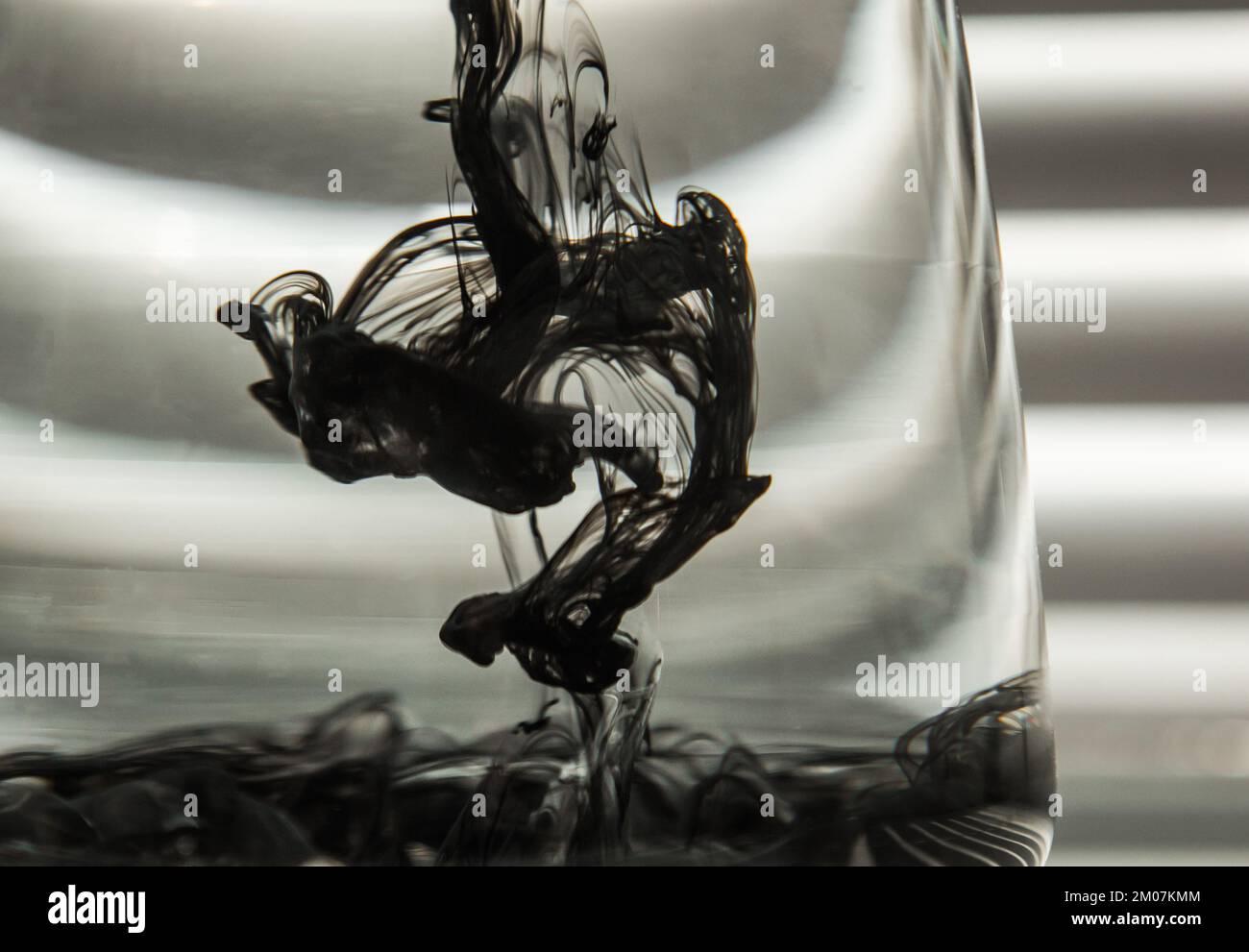 a cloud of ink in a transparent glass cup with clear water against the ...