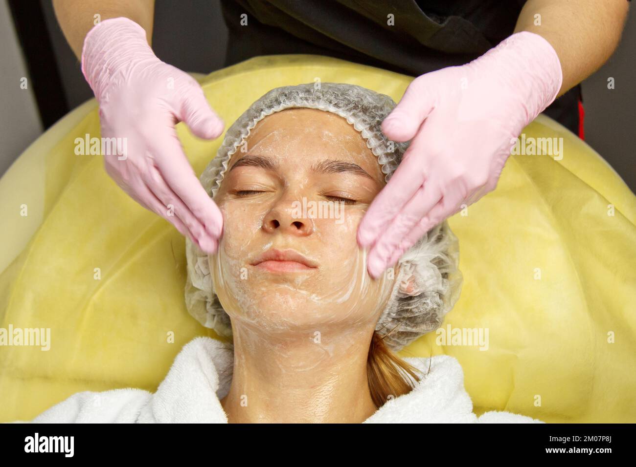 concept beautician. The hands of a cosmetologist put cream on the face of a woman. Beautician