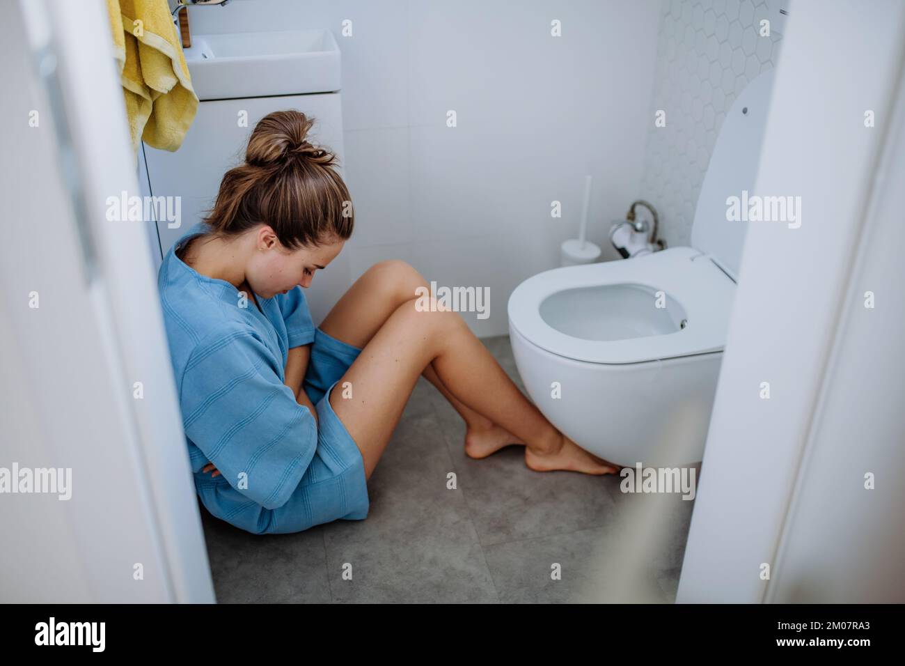 Young sick woman sitting on floor near toilet. Stock Photo