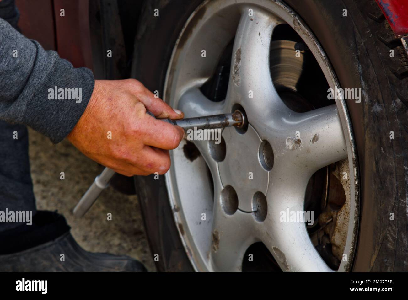 Auto mechanic man with electric screwdriver changing tire outside. Car