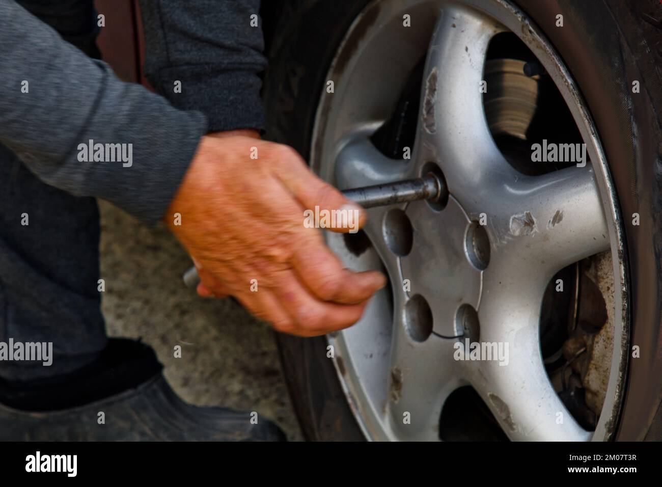 Auto mechanic man with electric screwdriver changing tire outside. Car