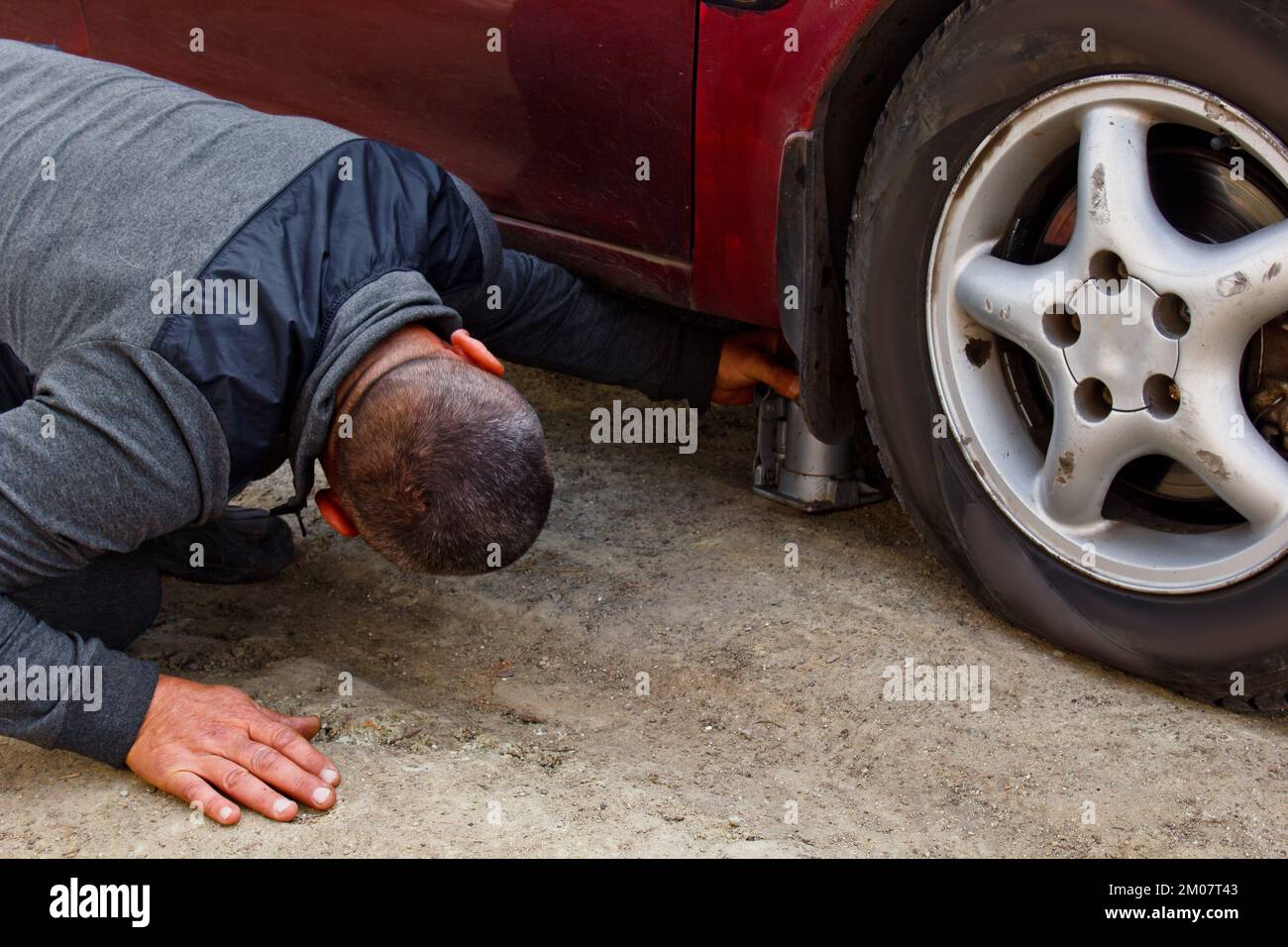 Auto mechanic man with electric screwdriver changing tire outside. Car