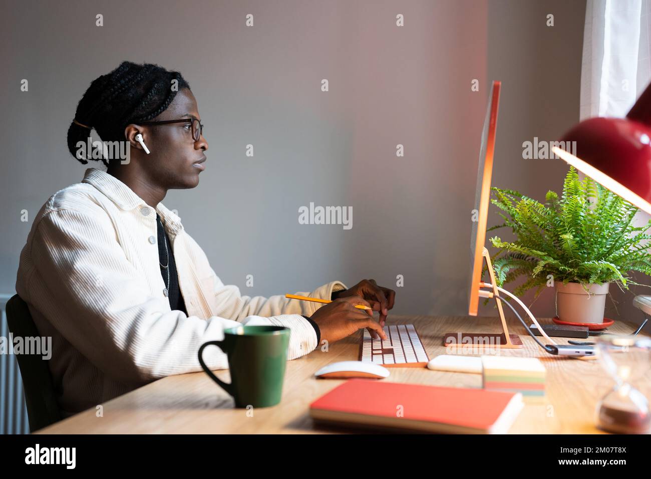 Focused African man freelance web developer writing code, using computer, sitting at home office Stock Photo
