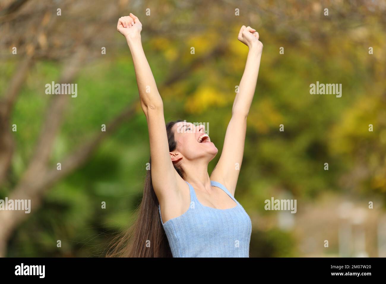 Excited teen raising arms celebrating success in a park Stock Photo