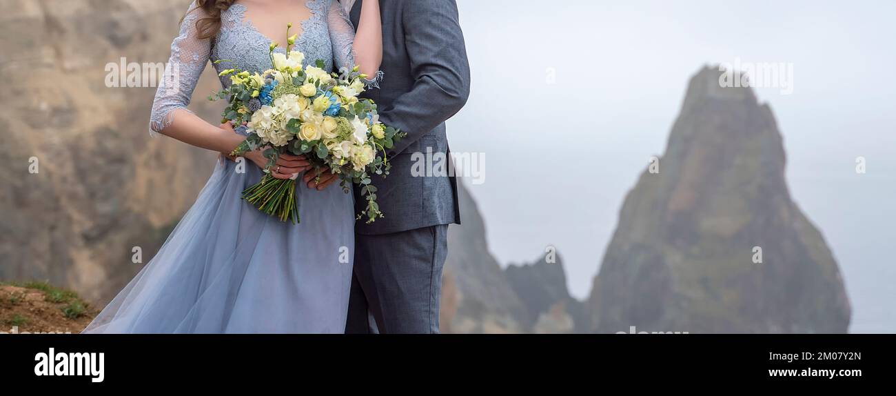 a couple standing in an embrace holding a beautiful bouquet of flowers, a girl dressed in a blue long dress, a man dressed in a suit. wedding concept Stock Photo