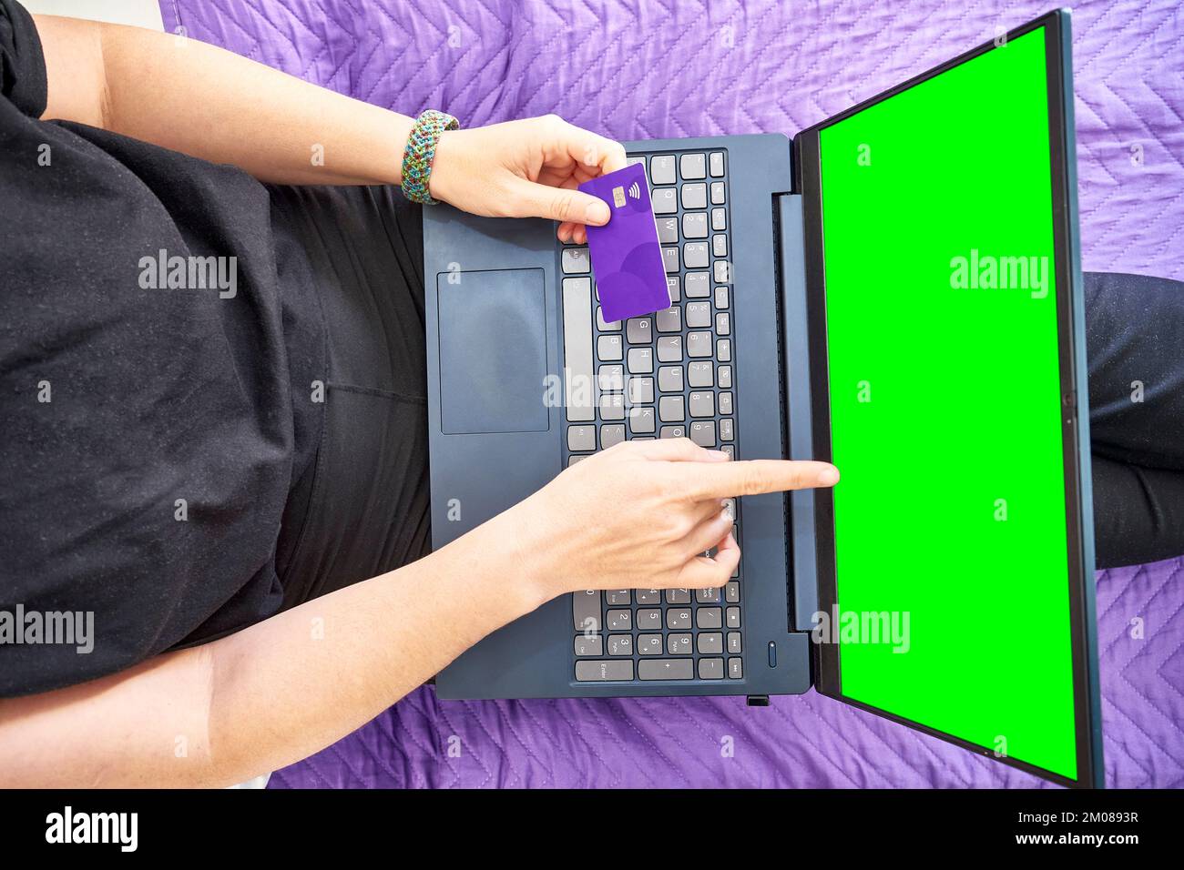 A top view of a person's hands pointing at the green screen of a laptop and holding a bank card Stock Photo