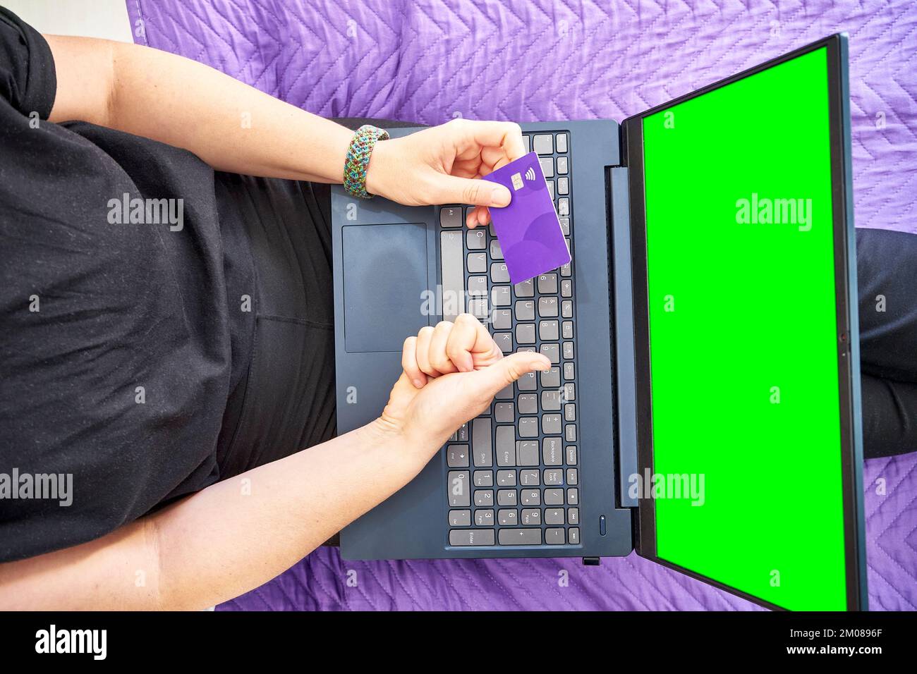 A top view of a person's hands pointing at the green screen of a laptop and holding a bank card Stock Photo