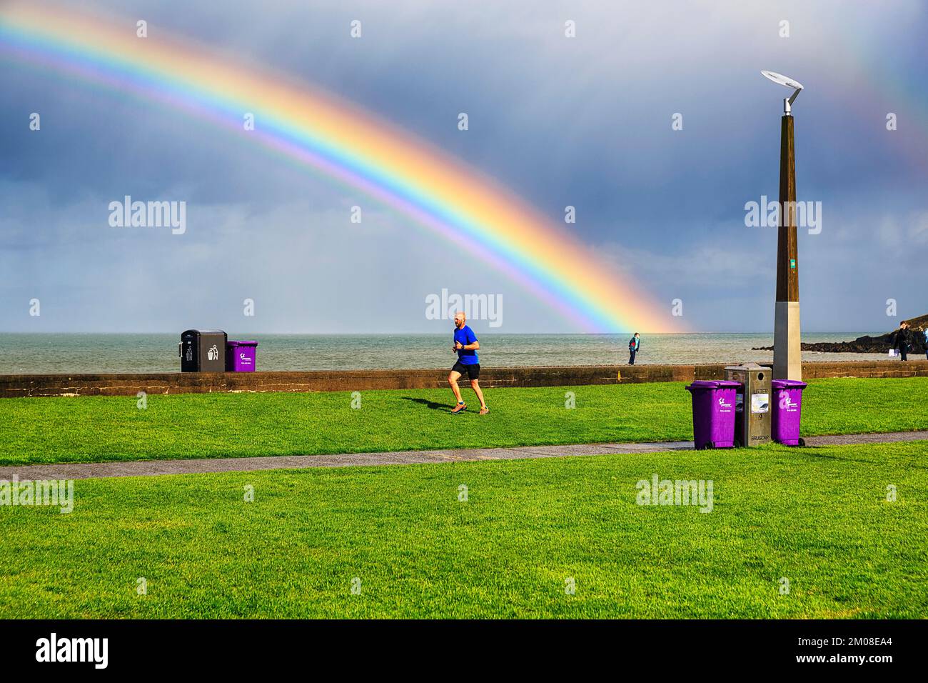 Pedestrians and joggers on seafront promenade, dramatic cloudy sky with rainbow, Bray, Wicklow, Ireland, Europe Stock Photo